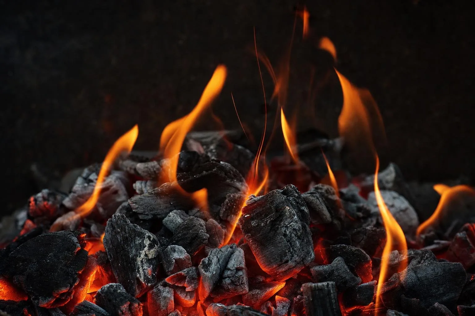 Macro of glowing charcoal embers with orange flames licking upward in darkness